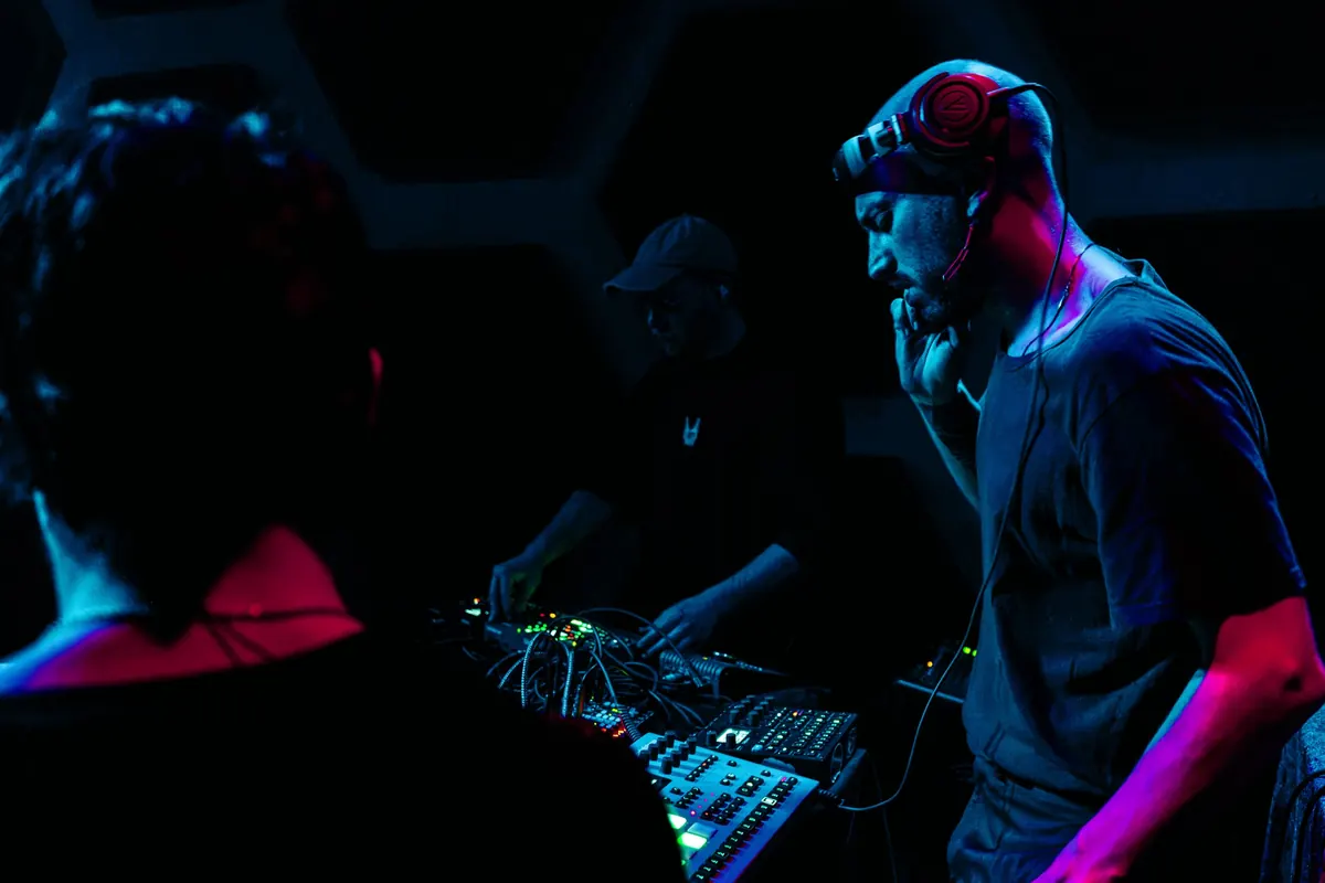 Performer with headphones at a hardware setup under blue and pink light